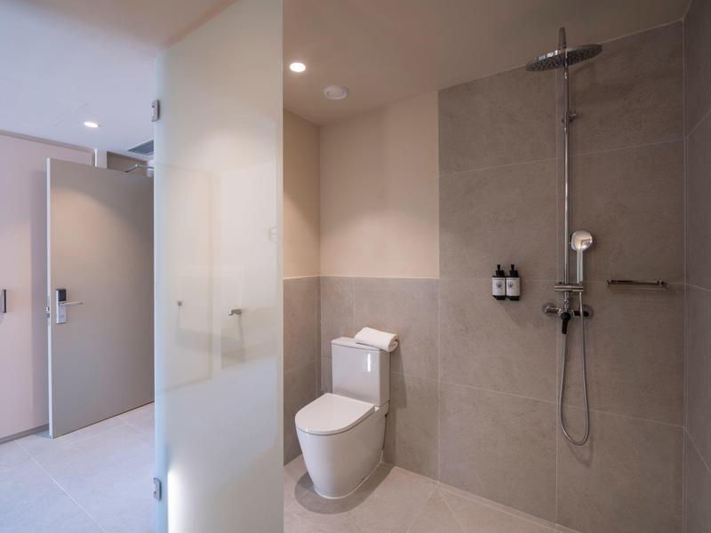 Baño moderno con ducha a ras de suelo, inodoro y azulejos claros para huéspedes del hotel.