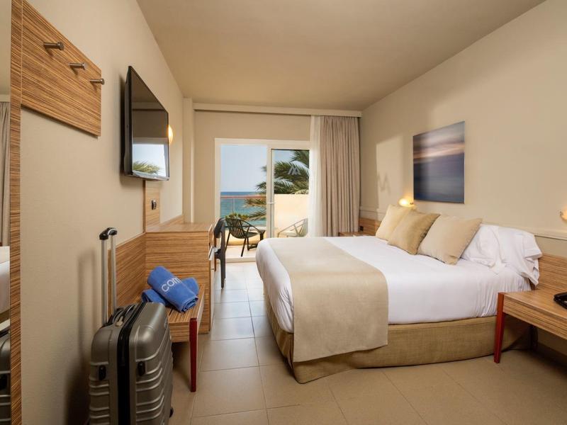 Habitación de hotel luminosa con cama doble, vista al mar y balcón, moderna y acogedora.