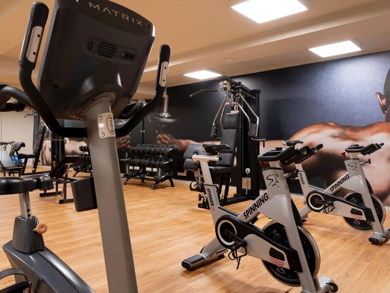 Equipos de gimnasio modernos en una sala de fitness bien iluminada con suelo de madera y decoración mural.