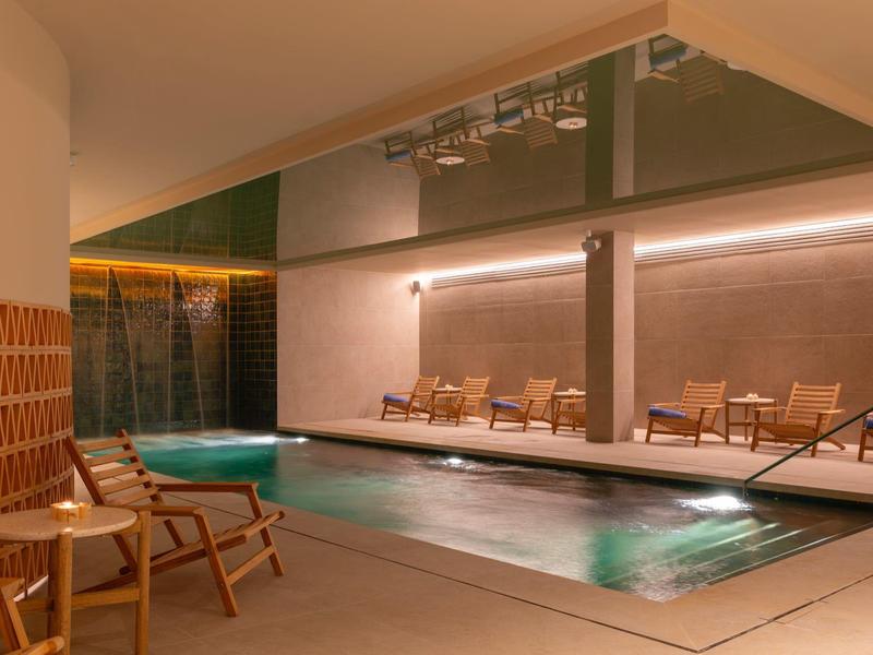 Área de piscina interior moderna con tumbonas y iluminación ambiental en un hotel.
