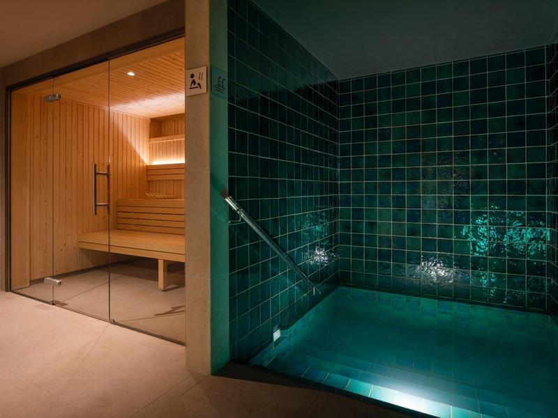 Área de sauna de diseño moderno con bancos de madera y piscina pequeña iluminada con azulejos verdes.