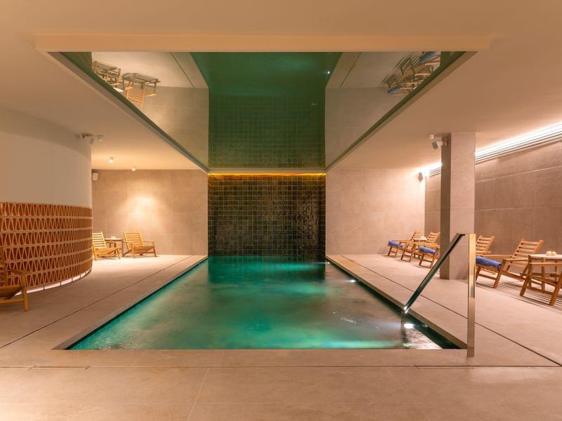 Piscina interior moderna con pared de cascada, muebles de madera acogedores y diseño de luz cálida.