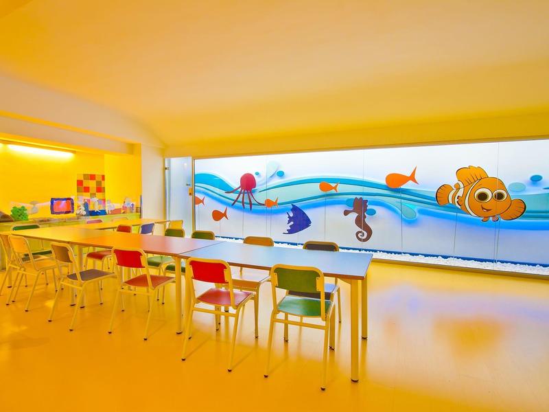 Sala de juegos colorida para niños con mesas, sillas y decoración de pared con animales marinos y pez payaso.