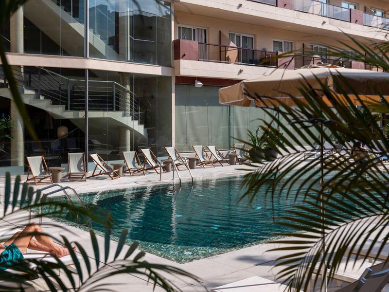 Piscina exterior moderna en un hotel con tumbonas y plantas en primer plano.