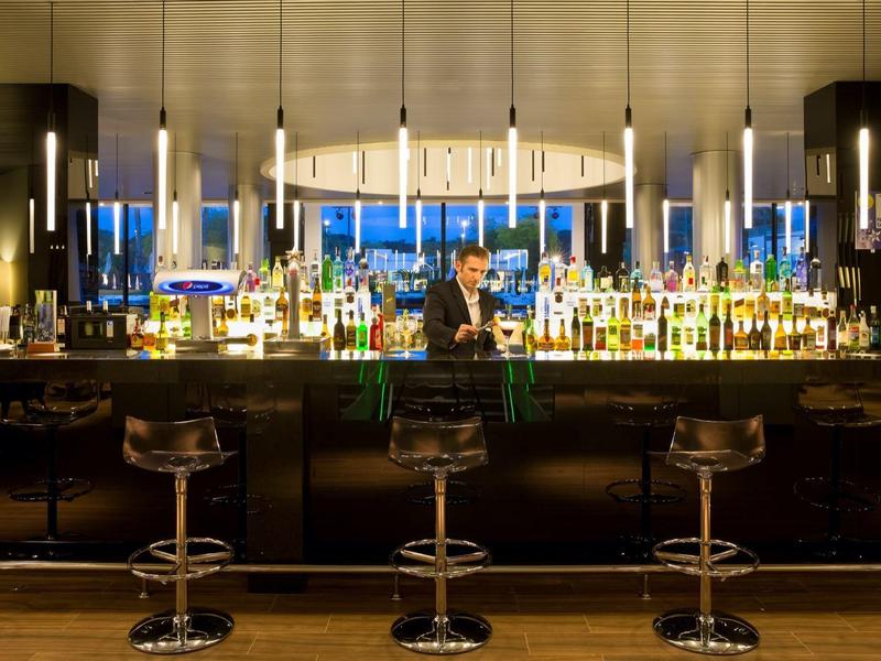 Elegante Bar mit glänzendem schwarzen Tresen, hohen Barhockern und moderner Beleuchtung bei Abenddämmerung.