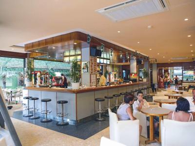 Modernes Café mit großen Fenstern, Holztheke, Barhockern und weißen Stühlen an Tischen.