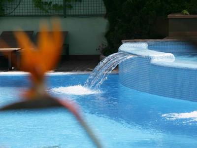 Blauer Pool mit Wasserspielen und verschwommener, orangefarbener Blüte im Vordergrund.