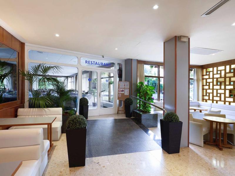 Bright hotel lobby area with plants, seating, and welcome sign at the entrance.