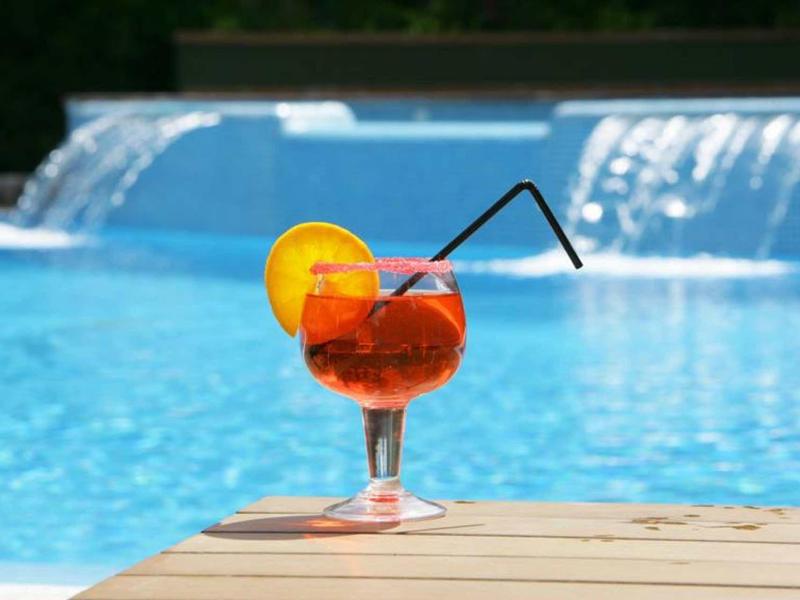 A refreshing cocktail with orange slice and straw on poolside in front of waterfalls.