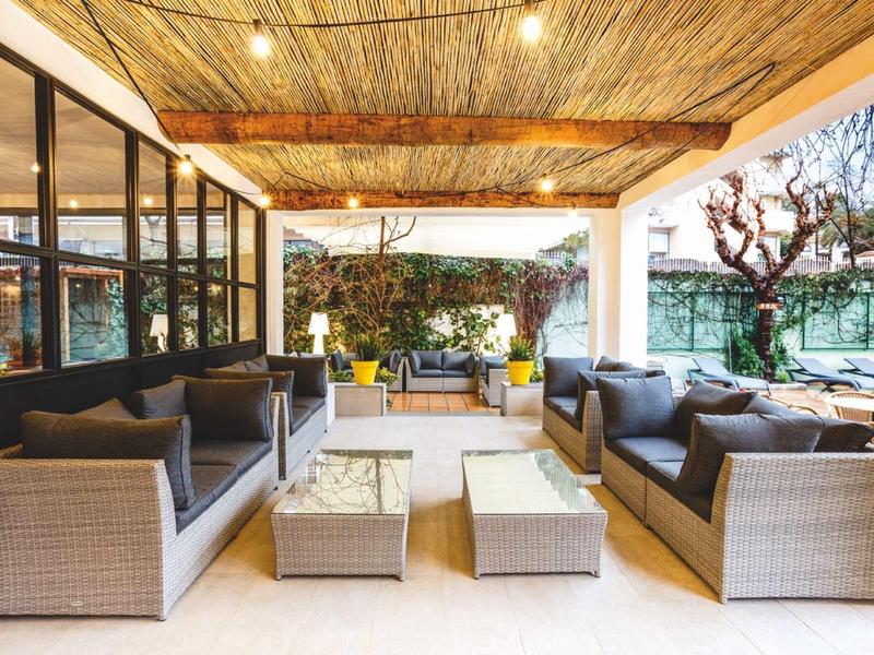 Cozy covered outdoor seating area with wicker furniture and glass walls in a hotel garden.