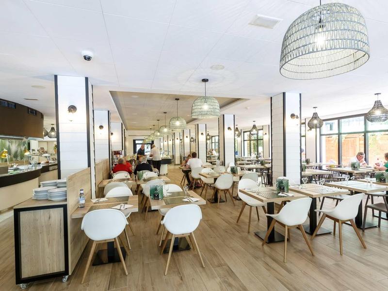 Bright, modern hotel restaurant with wooden floors and white chairs.