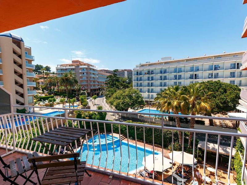 View from a balcony with chairs overlooking a hotel pool and surrounding buildings under clear sky.