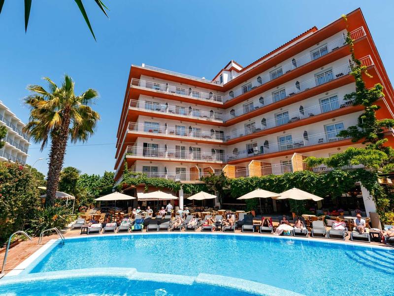 Modern hotel with pool, sun loungers, and palm trees under a blue sky.