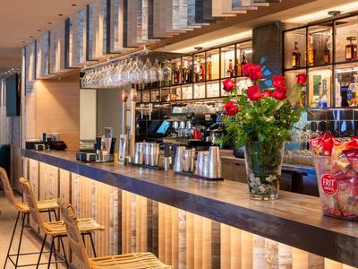 Moderner Hotelbarbereich mit Holztheke und Barhockern, dekoriert mit Blumen und Getränken.