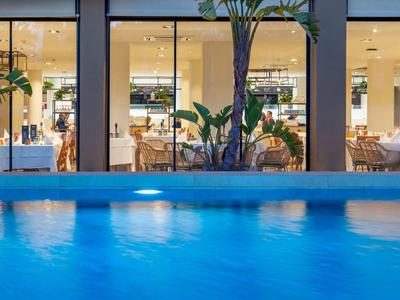 Moderner Hotelpool bei Nacht mit Blick auf gemütlich beleuchteten Speiseraum hinter großen Fenstern.