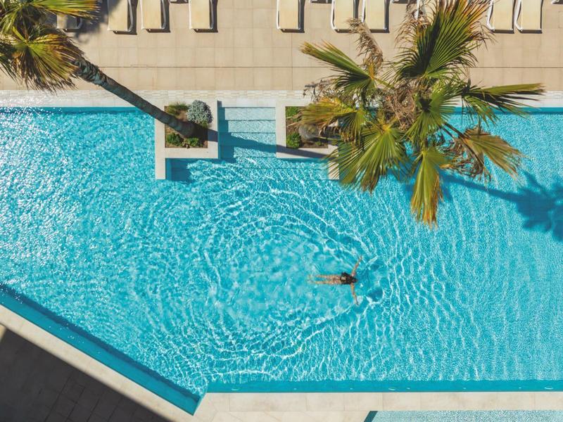 Blick von oben auf einen Swimmingpool mit Palmen und einer Person im Wasser.