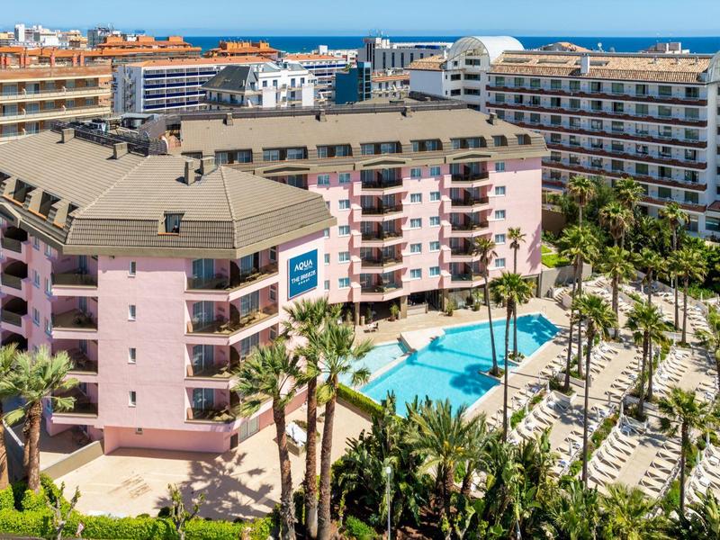 Großes Hotel mit mehreren Stockwerken, Swimmingpool und Palmen in einem sonnigen Urlaubsort.