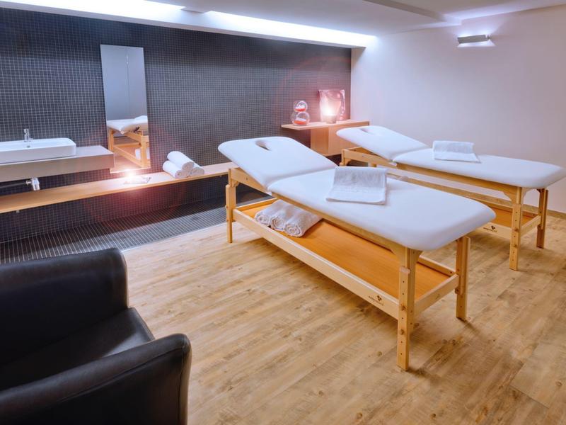 Heller Raum mit zwei Holz-Massageliegen, Holzboden, Waschtisch und entspanntem Ambiente.