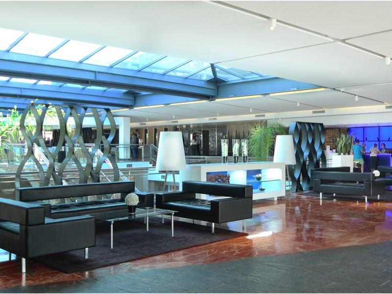 Moderne Lobby mit Glasdach, schwarzen Sofas, weißen Tischen und großen Pflanzen in weißen Töpfen.