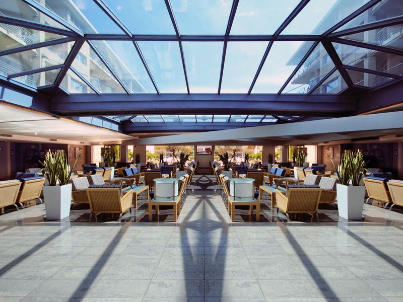 Hell erleuchteter, moderner Wintergarten mit Glasdach, Sesseln und Pflanzen in weißen Töpfen.