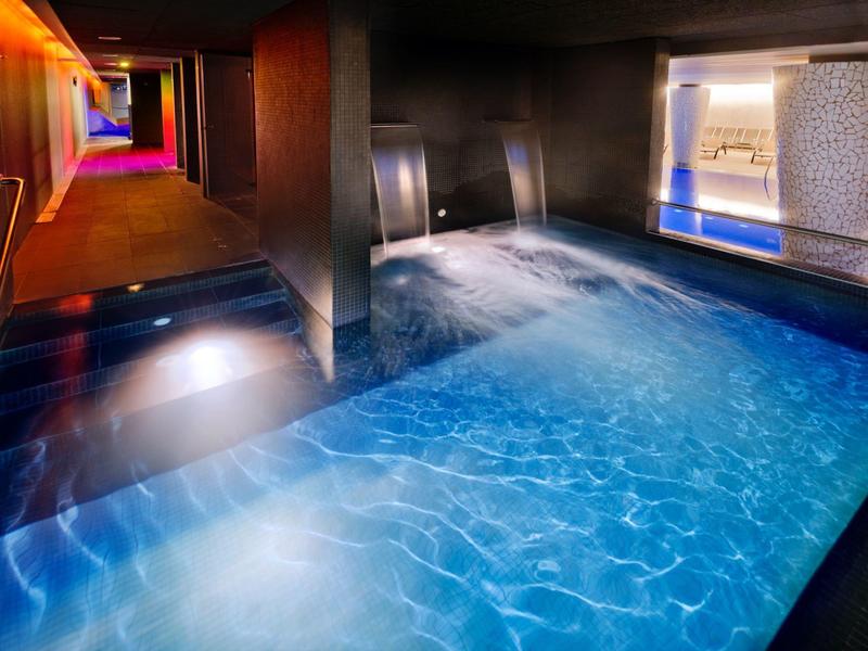 Innenraum mit beleuchtetem, klarem Wasserbecken und farbigem Flur im Hintergrund.