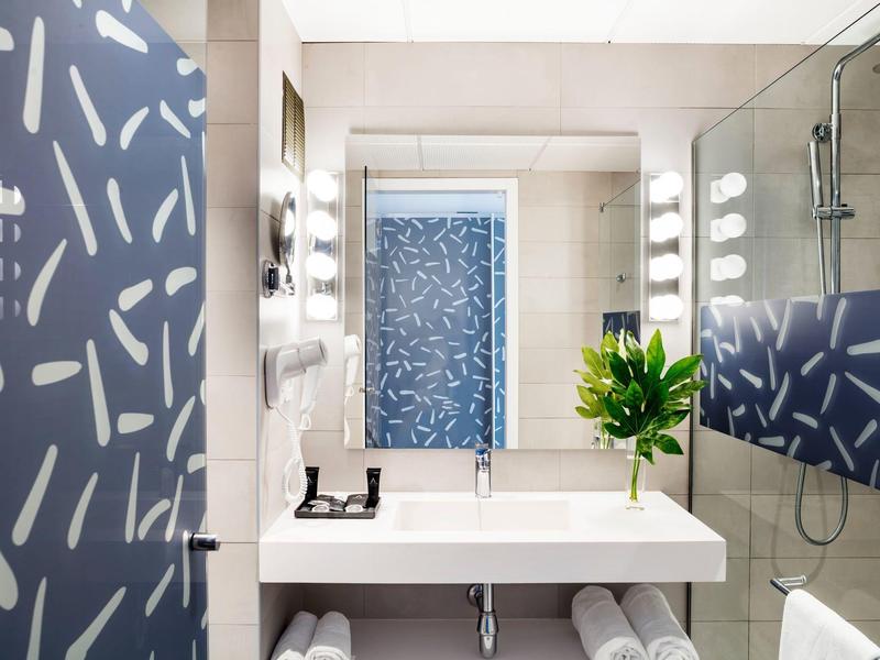 Modernes Badezimmer mit weißem Waschbecken, Spiegel, Glasdusche und blauer Tür mit hellem Muster.