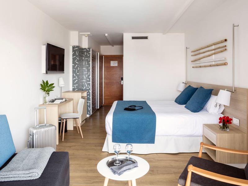 Helles, modern eingerichtetes Hotelzimmer mit Doppelbett, Schreibtisch, Sesseln und Fernseher.