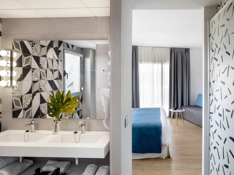 Modernes Badezimmer mit großem Spiegel, weißem Doppelwaschbecken und geometrischer Fliesenwand.