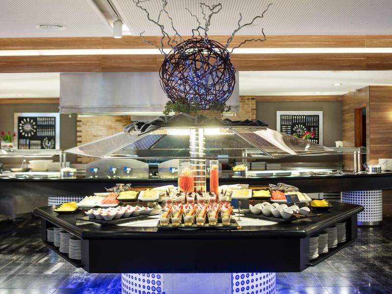 Buffet mit vielfältigen Speisen auf schwarzem Buffet-Tisch, darüber ein großer lila-ornamentaler Kronleuchter.