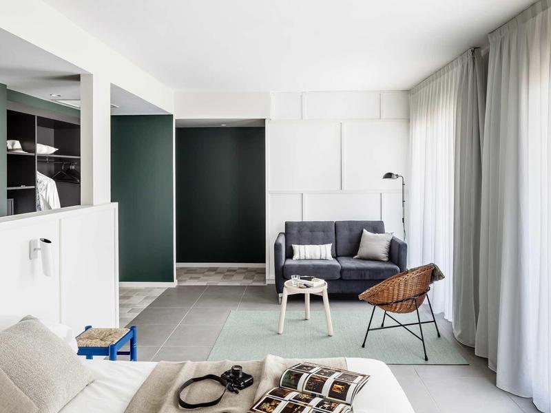 Sala de estar moderna con sofá gris, sillón y grandes ventanales con cortinas blancas.