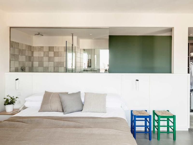 Dormitorio moderno con cama grande y vista a la cocina contigua a través de ventanas de vidrio.