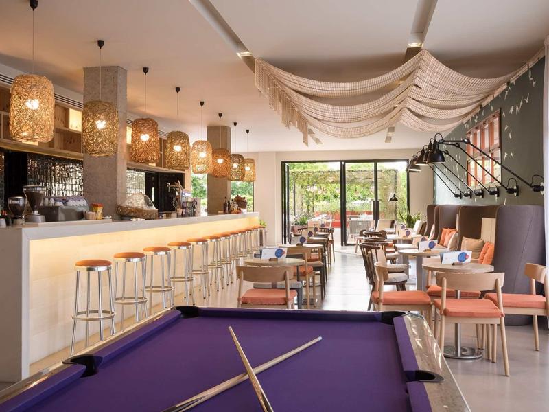 Sala moderna con bar, mesa de billar y áreas de estar en una zona luminosa del hotel.