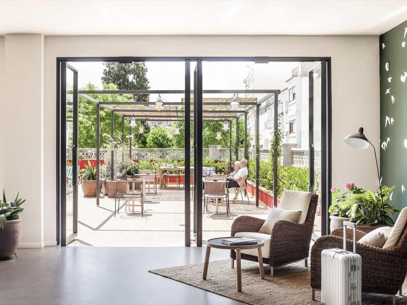 Sala luminosa de hotel con zona de estar y terraza abierta con vista al jardín a la luz del día.