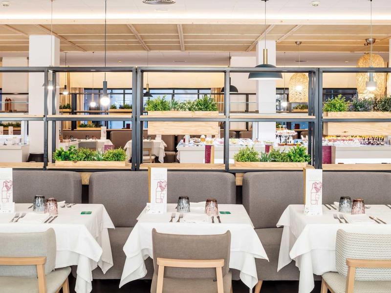 Restaurante moderno con mesas puestas, manteles blancos y sillas grises en ambiente luminoso.