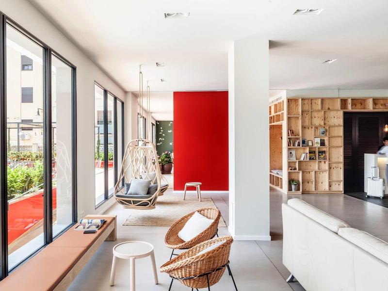 Lobby moderna de hotel con sillas, sillas colgantes y grandes ventanas con vista exterior.