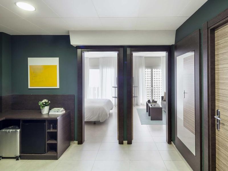 Pasillo moderno de hotel con puertas a dormitorios, esquina para sentarse y cuadro decorativo en la pared.