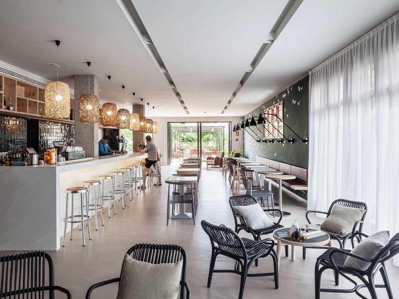 Interior moderno de bar de hotel con taburetes, sillones lounge y grandes ventanas con luz natural.