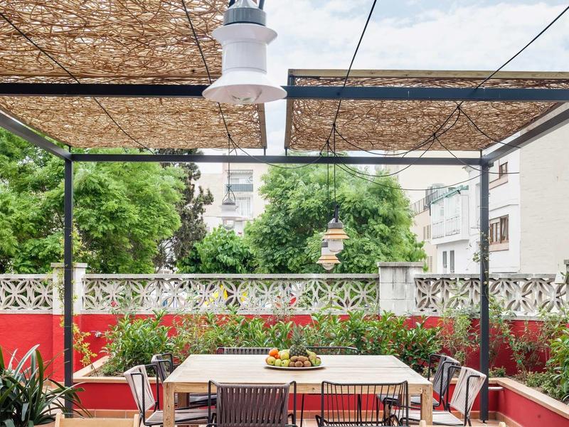 Terraza cubierta con mesa y sillas, rodeada de plantas y paredes rojas.