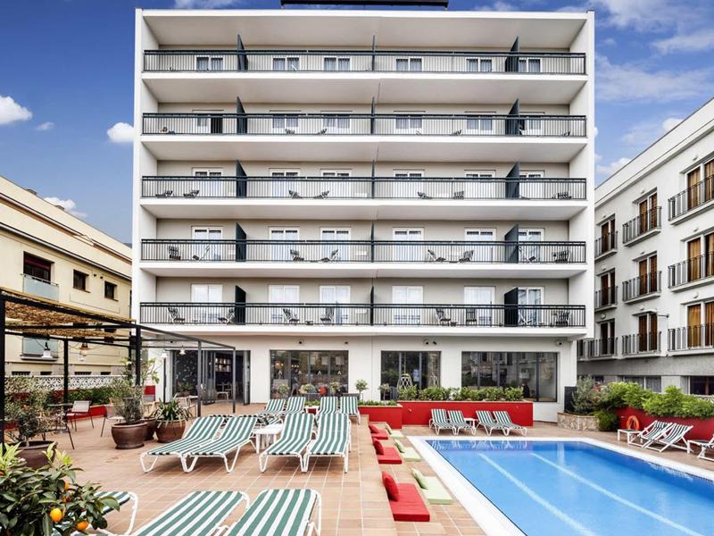 Hotel moderno de varios pisos con piscina y tumbonas en la terraza exterior.