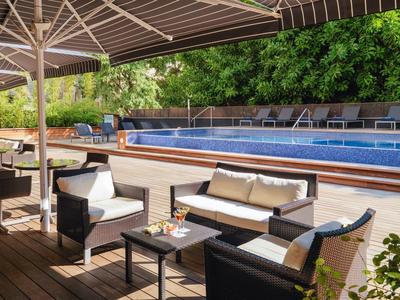 Moderne Terrasse mit Holzdeck, Sitzgruppen und großem Pool, umgeben von grünen Bäumen.