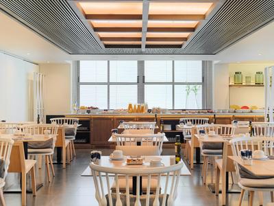 Moderner Frühstücksraum mit Holztischen, Stühlen und großen Fenstern, viel Licht und klarer Anordnung.