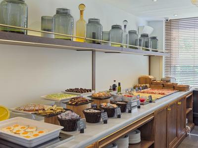 Buffet mit vielfältigen Speisen, Gläsern und Brotkorb auf langer Holztheke vor Fenster.