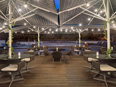 Moderner Außenbereich mit Holzterrasse, runden Tischen, Stühlen und beleuchteten weißen Sonnenschirmen.