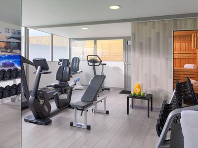 Salle de sport moderne avec équipements, haltères, sauna et coin salon avec grande fenêtre.