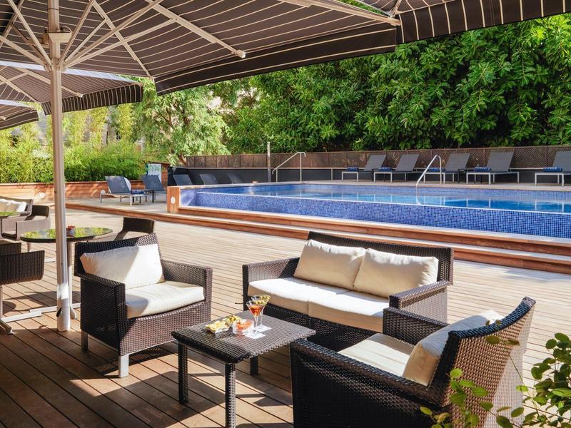 Moderne Terrasse mit Holzdeck, Sitzgruppen und großem Pool, umgeben von grünen Bäumen.