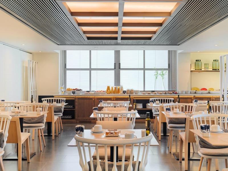 Moderner Frühstücksraum mit Holztischen, Stühlen und großen Fenstern, viel Licht und klarer Anordnung.