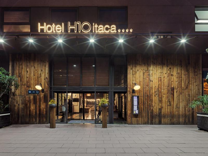 Eingang eines Hotels mit Holzverkleidung, Glasfront und beleuchtetem Schriftzug "Hotel HI Otaca".