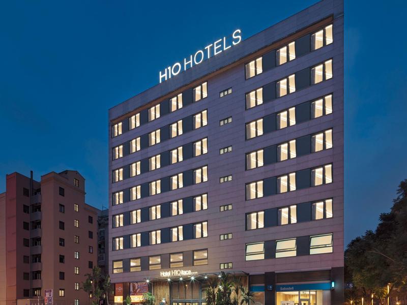 Fünfstöckiges Hotelgebäude mit beleuchteten Fenstern vor blauem Abendhimmel.