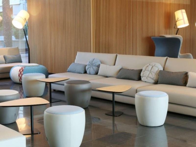 Wohnzimmer mit großen grauen Sofas, weißen Hockern, Holzwänden und modernen Stehlampen.