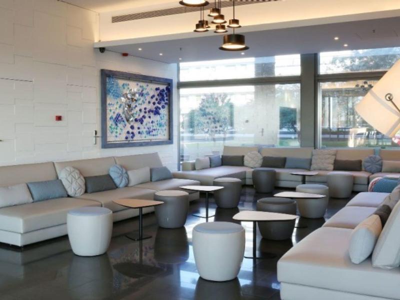 Heller, moderner Wohnraum mit grauen Sofas, weißen Hockern, Glasfenstern und Kunst an der Wand.